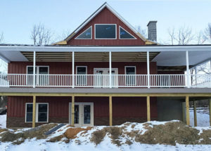 Large home with wrap around porch, new metal roof, red siding and brick facade.